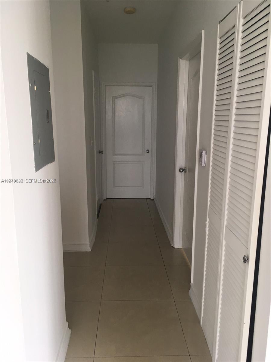 A narrow hallway features light-colored tile flooring, white doors, and a wall-mounted electrical panel — 5091 NW 7th St # 602, Miami FL 33126, MIAMI, FL