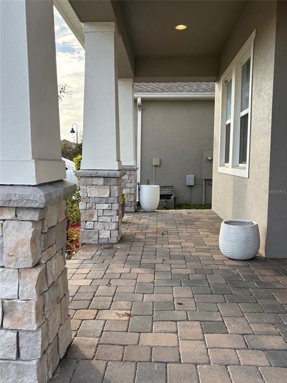 A covered front porch features stone-based columns, paver flooring, and two white decorative planters — 1872 IBIS BAY COURT, OCOEE, FL
