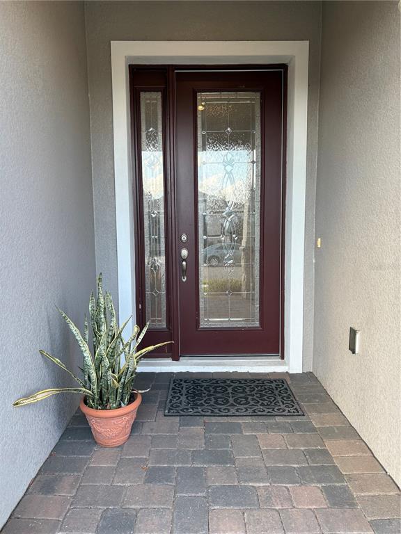 A dark red front door with a glass panel and sidelight sits on a paved porch — 1872 IBIS BAY COURT, OCOEE, FL