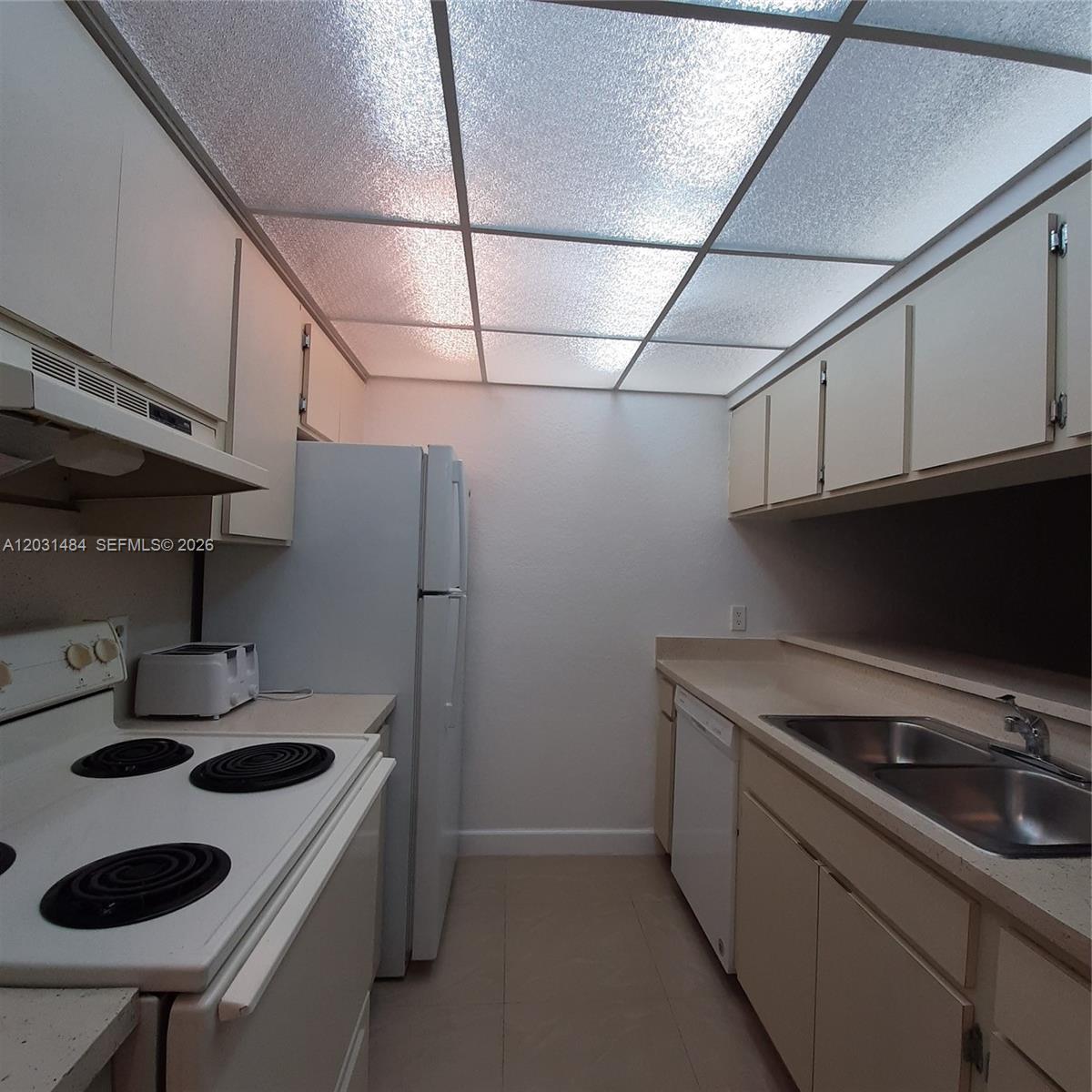 A galley kitchen features white appliances, beige cabinets, and a textured drop ceiling — 8160 GENEVA WY # 316, Miami FL 33166, MIAMI, FL