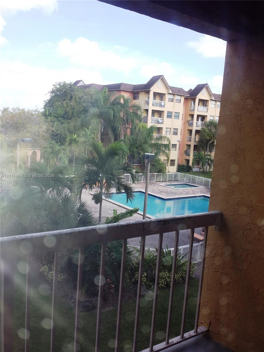 A balcony view overlooks a swimming pool, palm trees, and a multi-story apartment building — 8160 GENEVA WY # 316, Miami FL 33166, MIAMI, FL