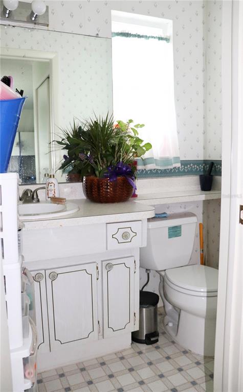 A bathroom features a white vanity, a toilet, a mirror, and floral wallpaper — 6990 VERSAILLES N UNIT 6990, PINELLAS PARK, FL