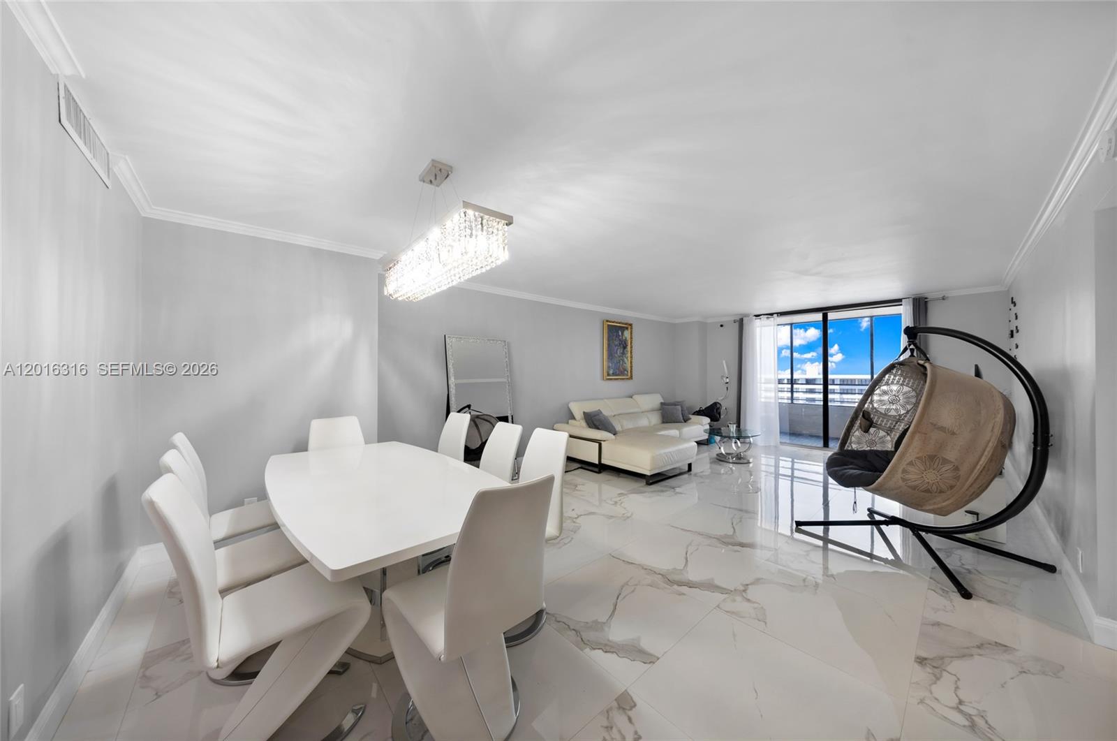 A dining and living area features white marble floors, a crystal chandelier, and a hanging chair — 2500 Parkview Dr # 2119, Hallandale Beach FL 33009, HALLANDALE BEACH, FL
