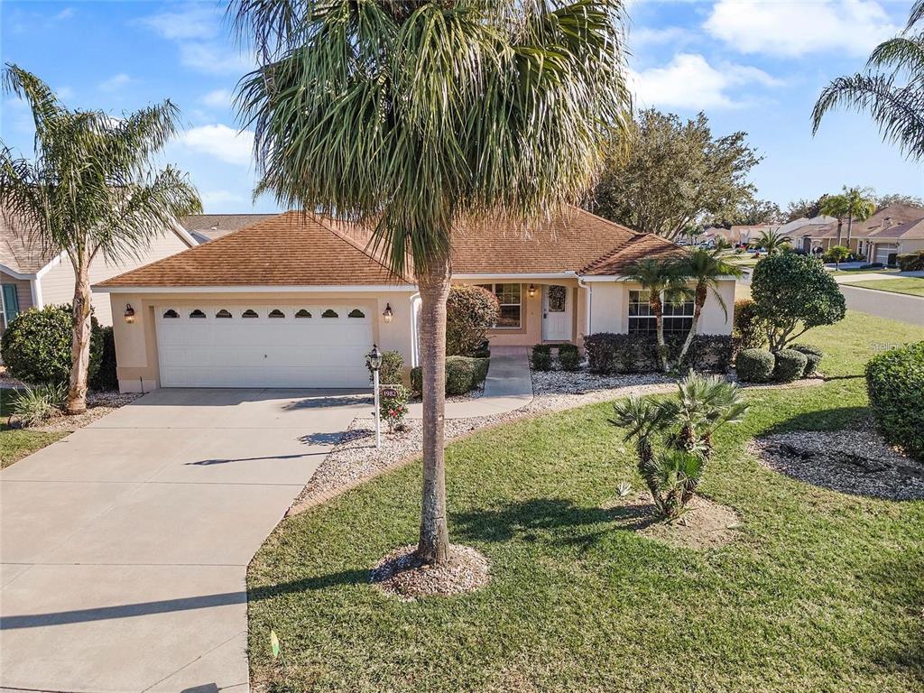 A single-story house with a two-car garage, a palm tree, and a landscaped front yard — 1982 SOMERSET AVENUE, THE VILLAGES, FL