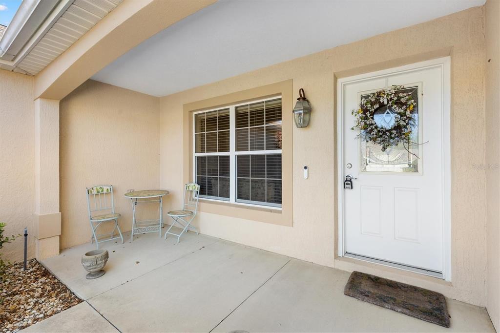A covered front porch with a white door, a window, and a small bistro set — 1982 SOMERSET AVENUE, THE VILLAGES, FL