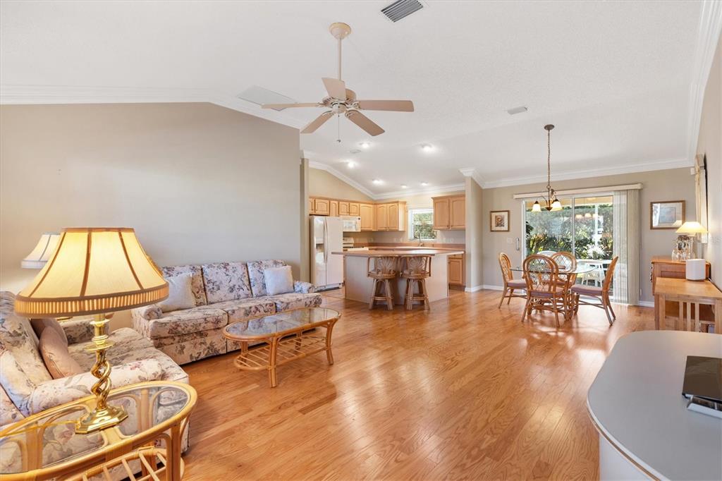 An open-concept living and dining area features hardwood floors, a vaulted ceiling, and kitchen cabinetry — 1982 SOMERSET AVENUE, THE VILLAGES, FL