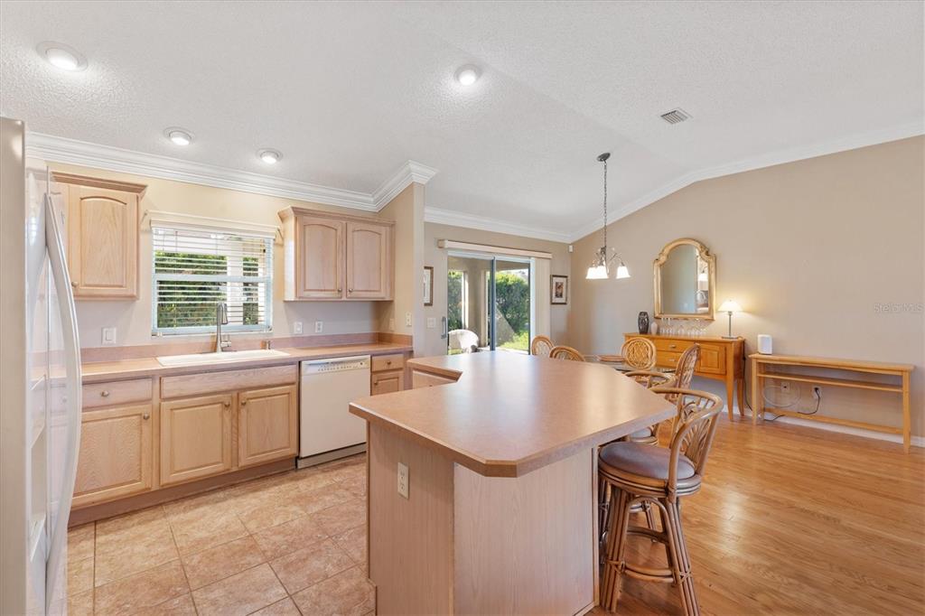 A kitchen with light wood cabinets, a central island, and an adjacent dining area — 1982 SOMERSET AVENUE, THE VILLAGES, FL