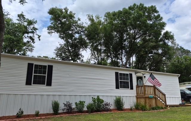A white manufactured home features black shutters, a wooden front porch, and an American flag — 2521 E MERCURY STREET, INVERNESS, FL