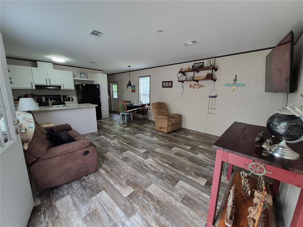 An open-concept living room and kitchen area with wood-look flooring and coastal decor — 2521 E MERCURY STREET, INVERNESS, FL
