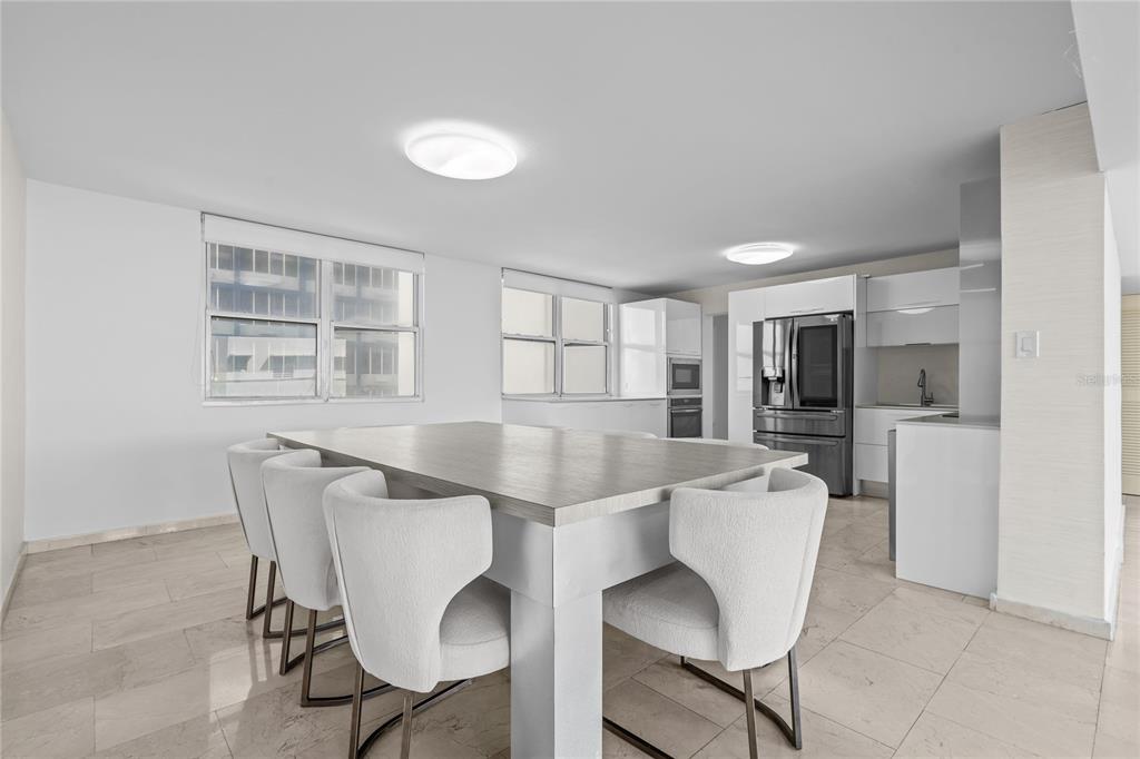 A modern dining area features a large table, upholstered chairs, and an adjacent white kitchen — #6 MARIANO RAMÍREZ BAGES - LAGUNA TERRACE UNIT 1, SAN JUAN, PR