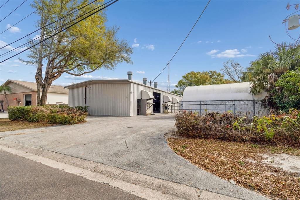 A metal industrial building stands next to a fenced-in white structure on a paved lot — 1060 HARBOR LAKE DRIVE, SAFETY HARBOR, FL