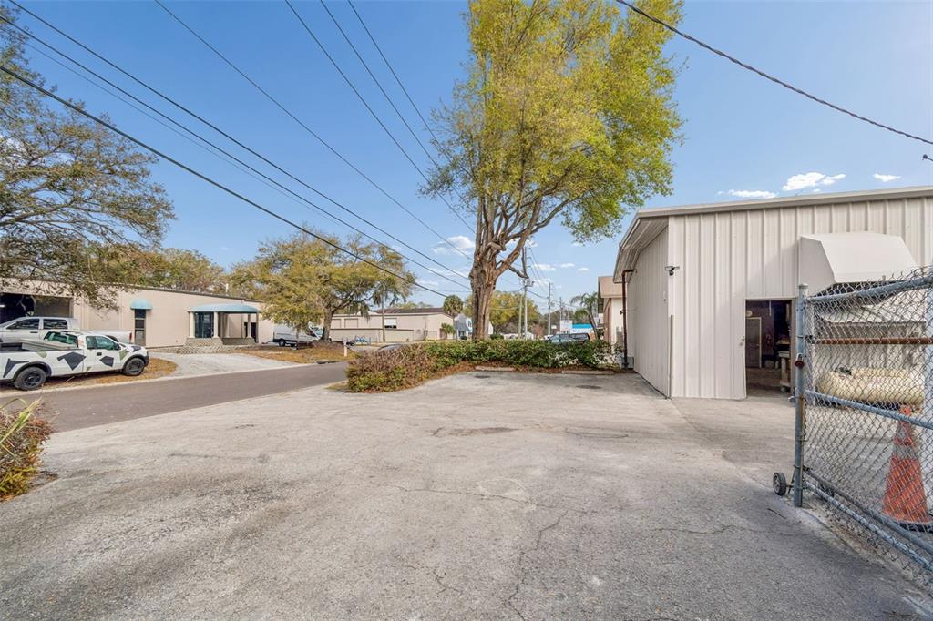 An outdoor paved parking area sits between two industrial buildings with a large tree nearby — 1060 HARBOR LAKE DRIVE, SAFETY HARBOR, FL