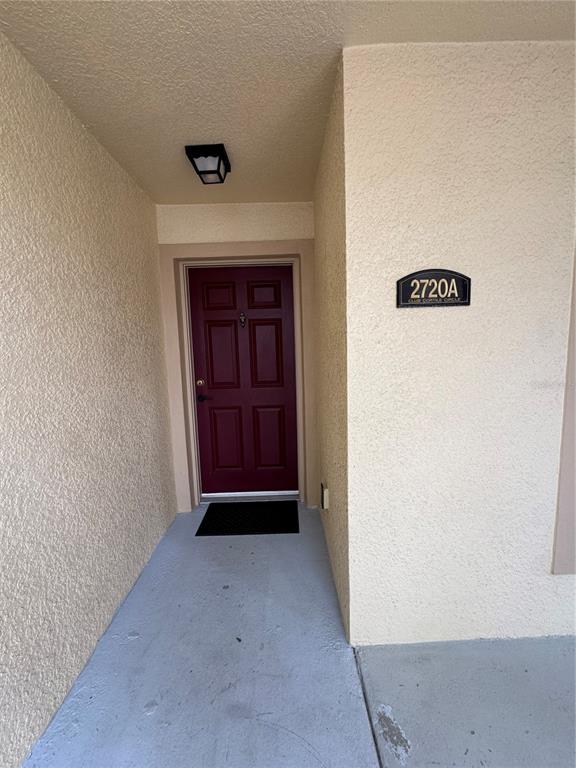 A maroon front door is recessed into a beige stucco entryway with a porch light — 2720 CLUB CORTILE CIRCLE UNIT A, KISSIMMEE, FL