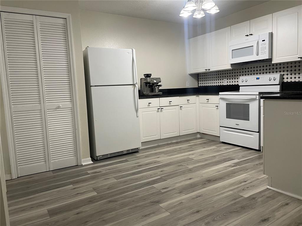 A kitchen features white cabinets, black countertops, a white refrigerator, and wood-look flooring — 2720 CLUB CORTILE CIRCLE UNIT A, KISSIMMEE, FL