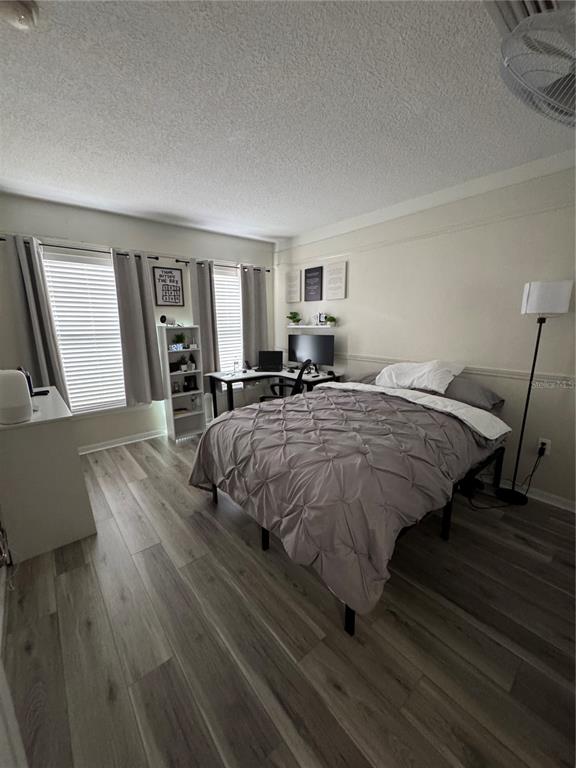 A bedroom features light wood-look flooring, a bed with a grey comforter, and a corner desk — 2720 CLUB CORTILE CIRCLE UNIT A, KISSIMMEE, FL