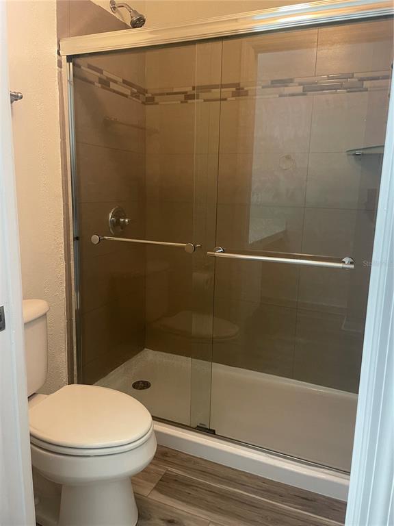 A bathroom features a white toilet next to a glass-enclosed shower with tiled walls — 2720 CLUB CORTILE CIRCLE UNIT A, KISSIMMEE, FL