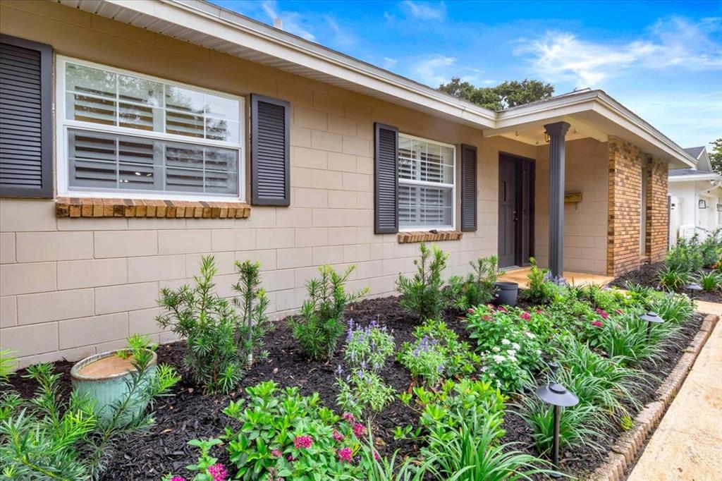 The exterior of a single-story house features tan block walls, dark shutters, and a landscaped garden — 715 S RANGER BOULEVARD, WINTER PARK, FL