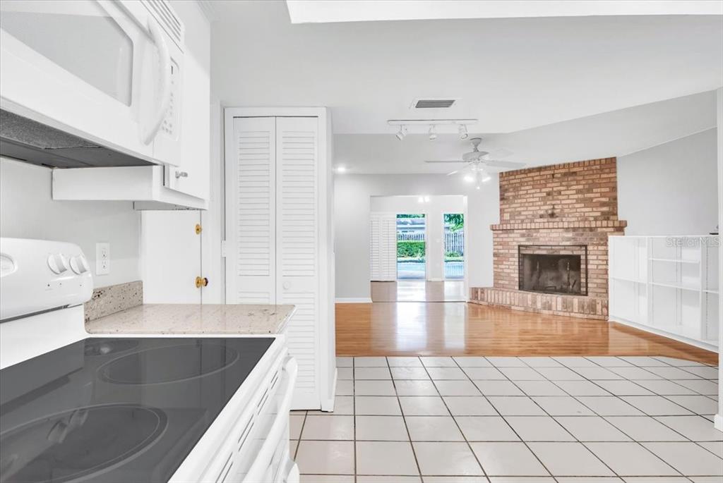 A kitchen with white appliances overlooks a living room featuring a brick fireplace — 715 S RANGER BOULEVARD, WINTER PARK, FL