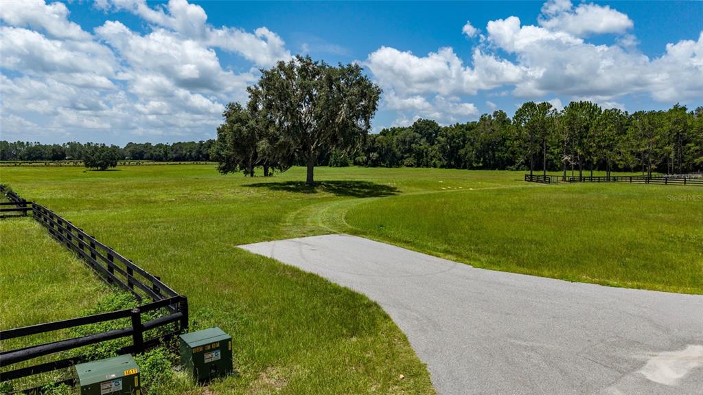 A paved driveway leads into a large, grassy field with a fence and trees — SE 159TH LN., SUMMERFIELD, FL