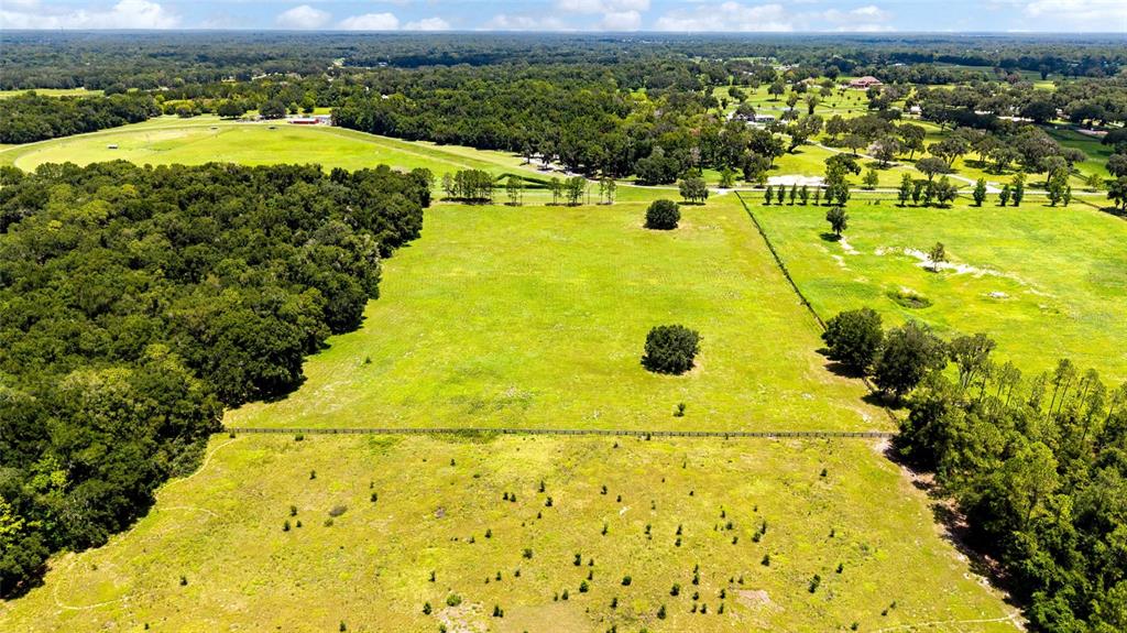 An aerial view shows a large, fenced grassy pasture bordered by dense woods and trees — SE 159TH LN., SUMMERFIELD, FL