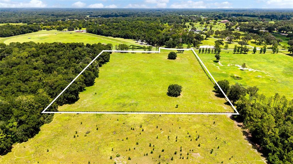 An aerial view shows a large, rectangular fenced pasture surrounded by trees and fields — SE 159TH LN., SUMMERFIELD, FL