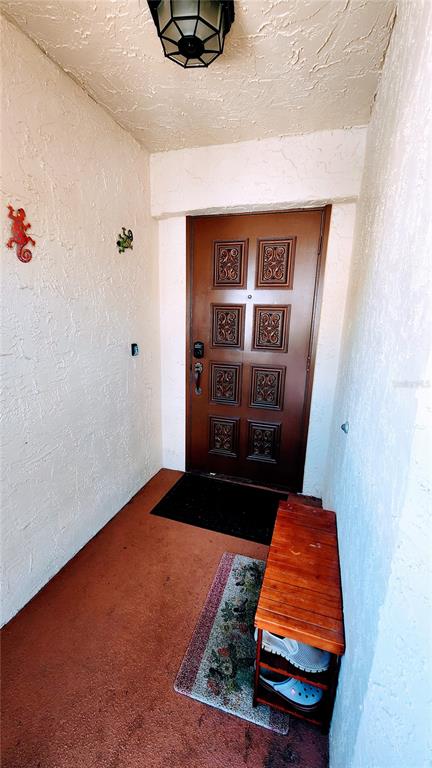 An entryway features a brown paneled door, a wooden shoe rack, and lizard wall decor — 6101 34TH STREET W UNIT 31H, BRADENTON, FL