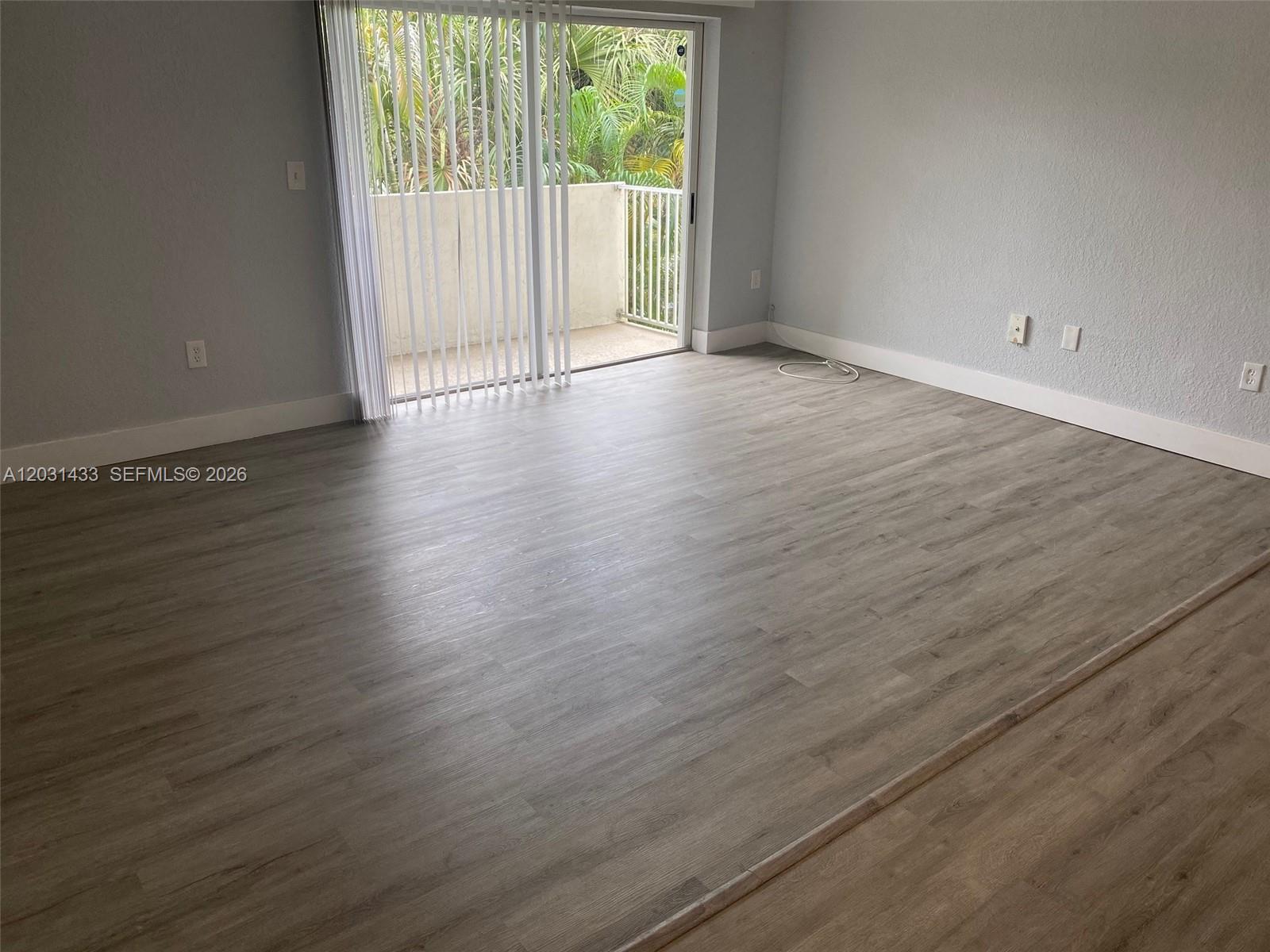An empty room features light wood-look flooring, gray walls, and a sliding glass door to a balcony — 8950 SW 69th Ct # 308, Pinecrest FL 33156, PINECREST, FL