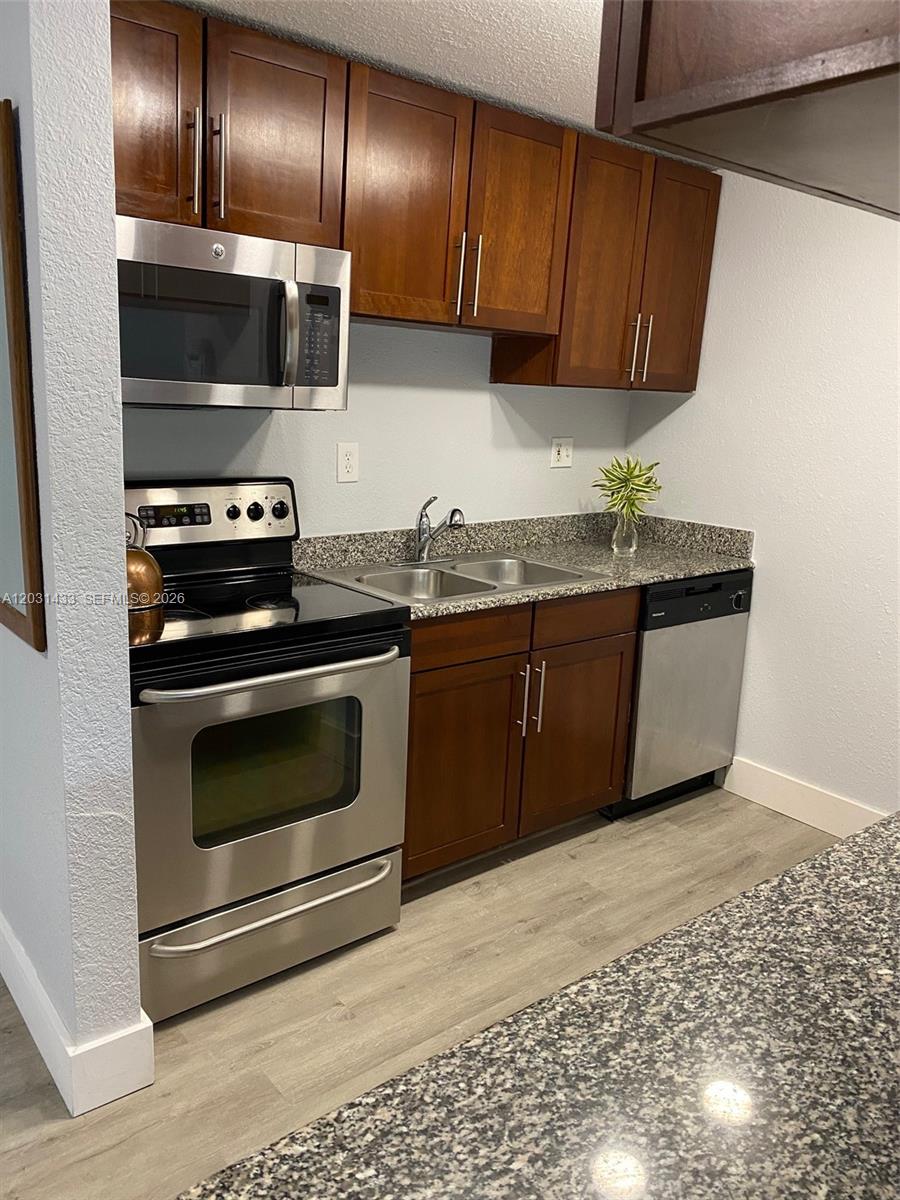 A kitchen features dark wood cabinets, stainless steel appliances, and granite countertops — 8950 SW 69th Ct # 308, Pinecrest FL 33156, PINECREST, FL