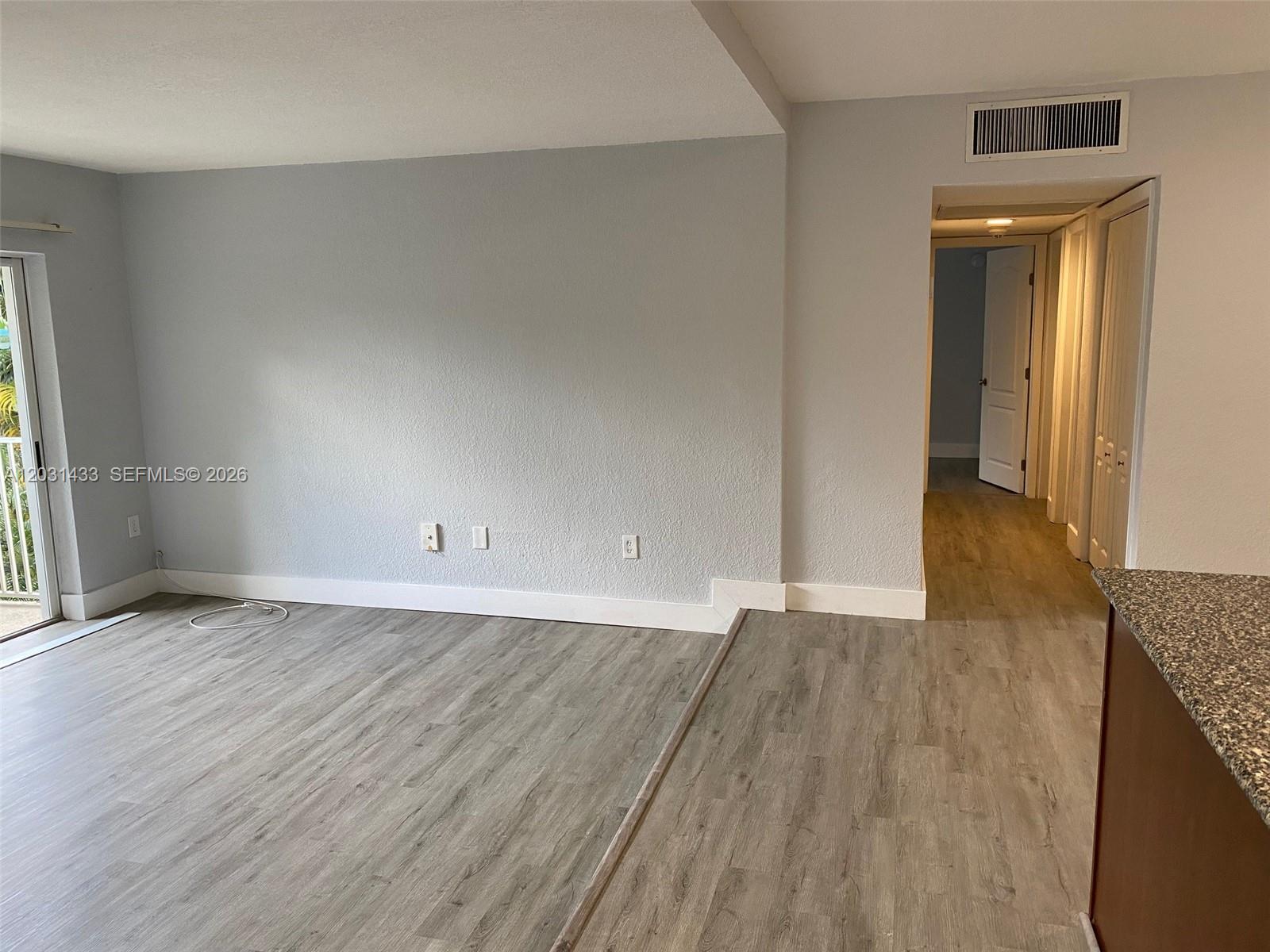 An empty living room features light gray walls, wood-look flooring, and a sliding glass door — 8950 SW 69th Ct # 308, Pinecrest FL 33156, PINECREST, FL