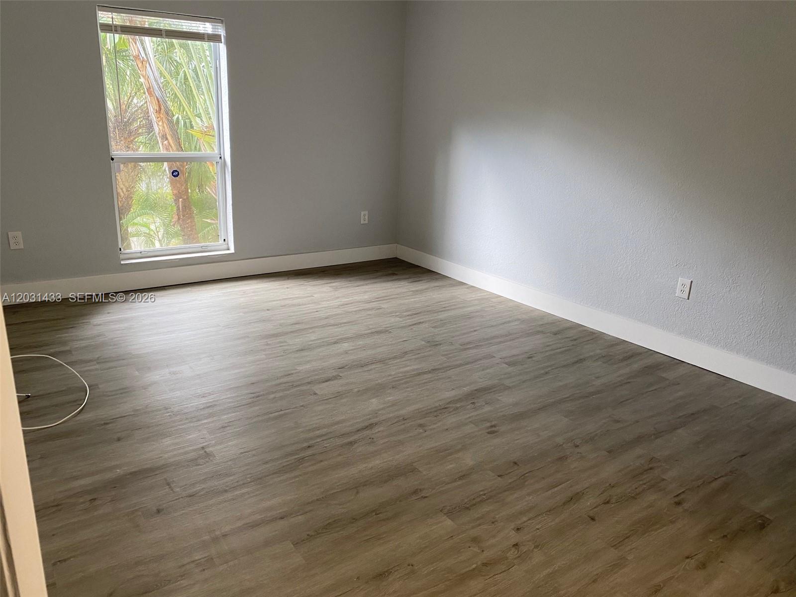 An empty room features light gray walls, white baseboards, and wood-look vinyl plank flooring — 8950 SW 69th Ct # 308, Pinecrest FL 33156, PINECREST, FL