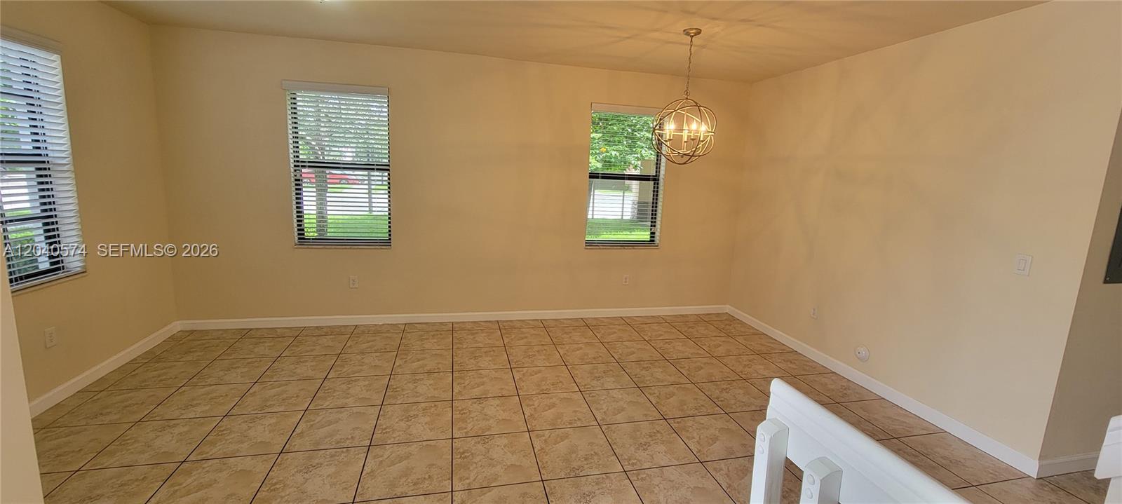An empty dining room features beige tile flooring, light-colored walls, and a spherical chandelier — 8872 W 35th Ct, Hialeah FL 33018, HIALEAH, FL