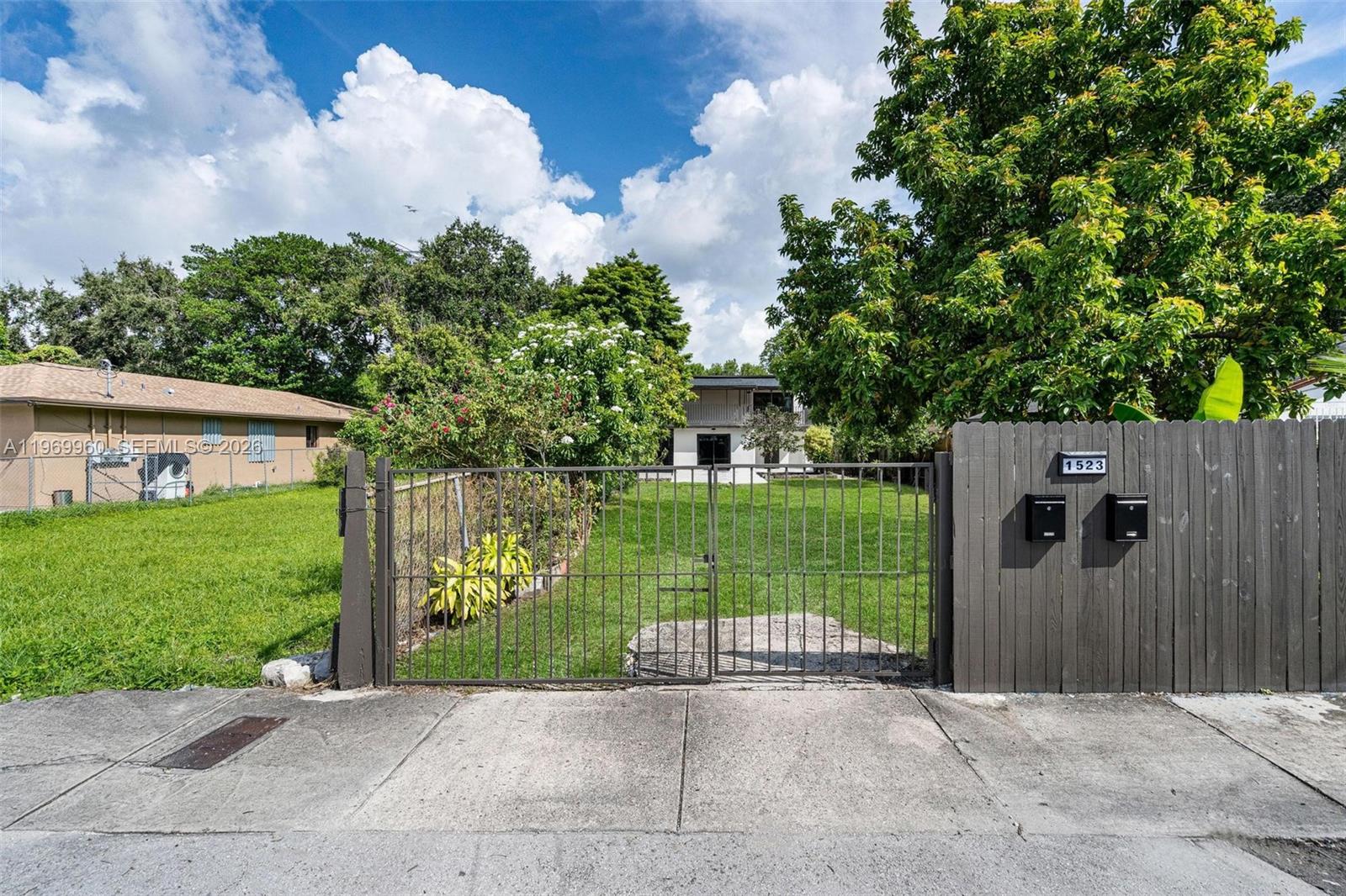A gated entrance leads to a grassy front yard with a house in the background — 1523 NW 38th St, Miami FL 33142, MIAMI, FL