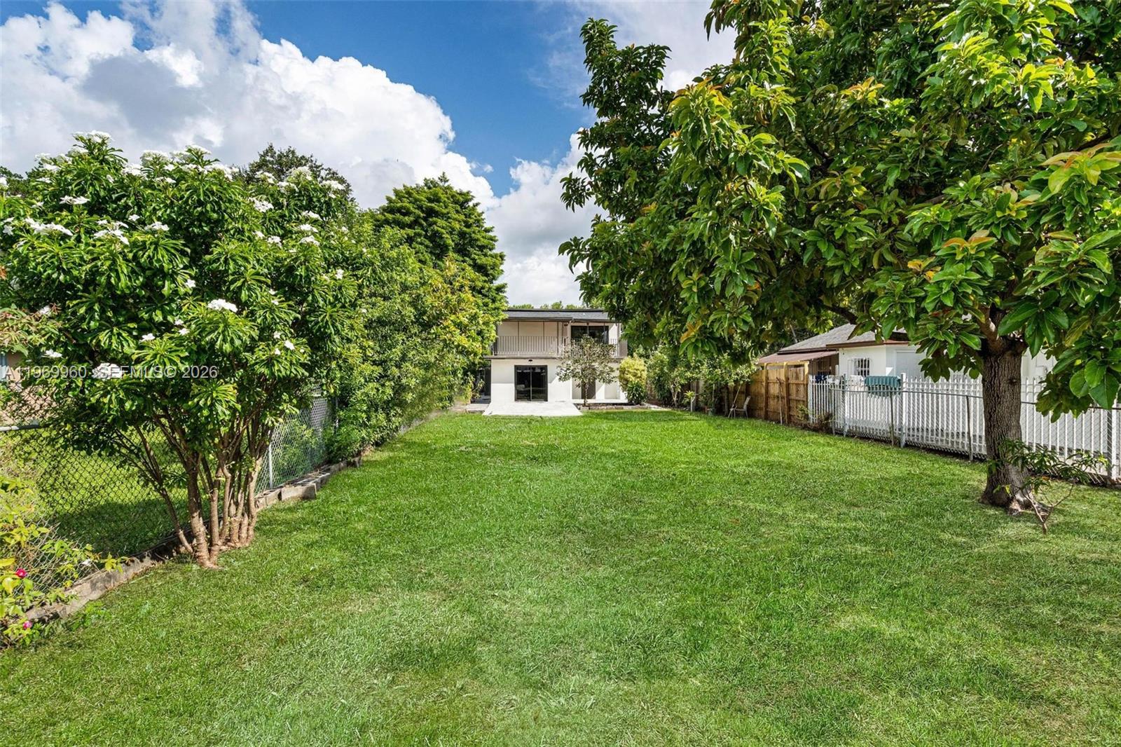 A grassy backyard features a large tree on the right and a two-story house beyond — 1523 NW 38th St, Miami FL 33142, MIAMI, FL