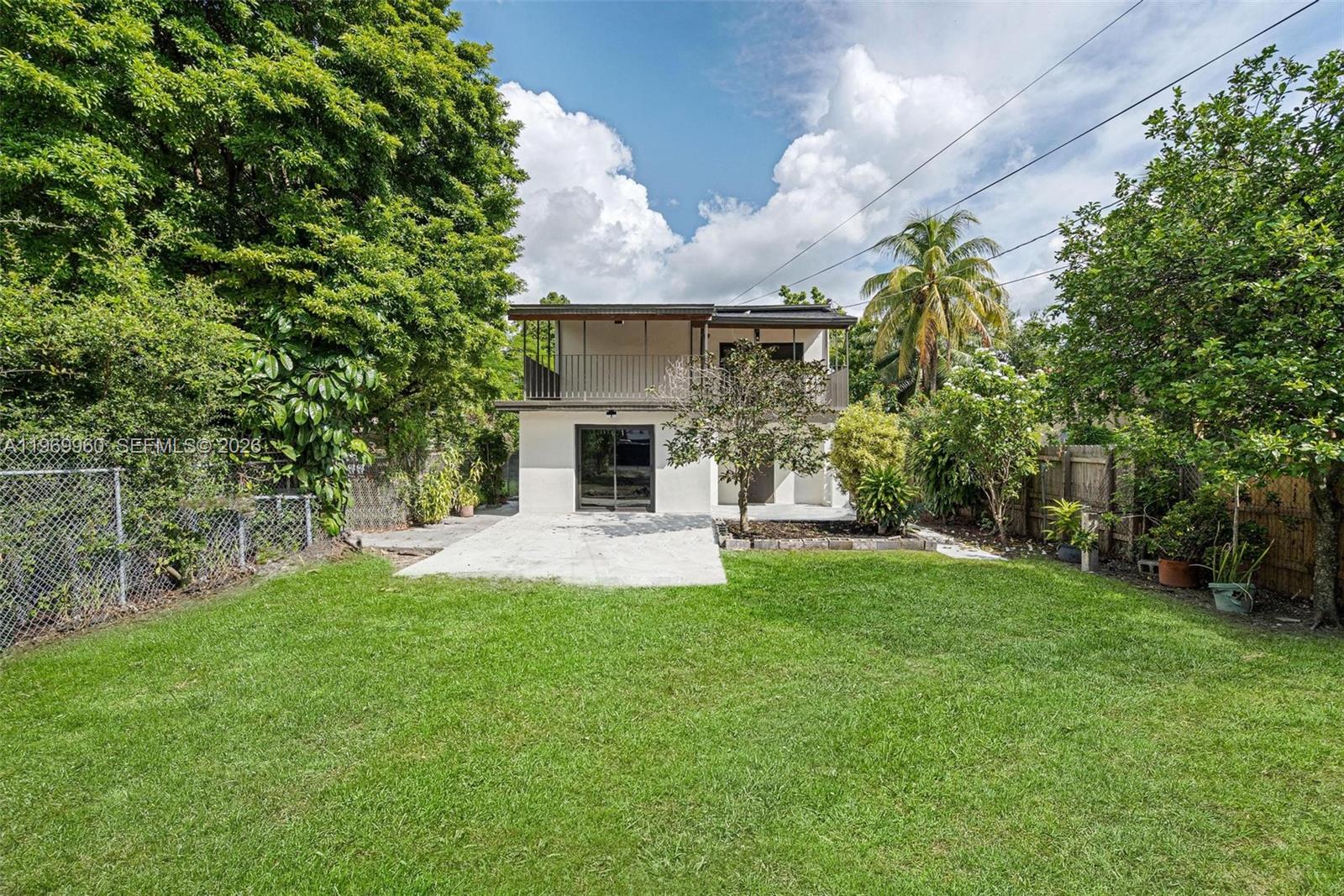A two-story house with a balcony and a concrete patio overlooks a grassy backyard — 1523 NW 38th St, Miami FL 33142, MIAMI, FL