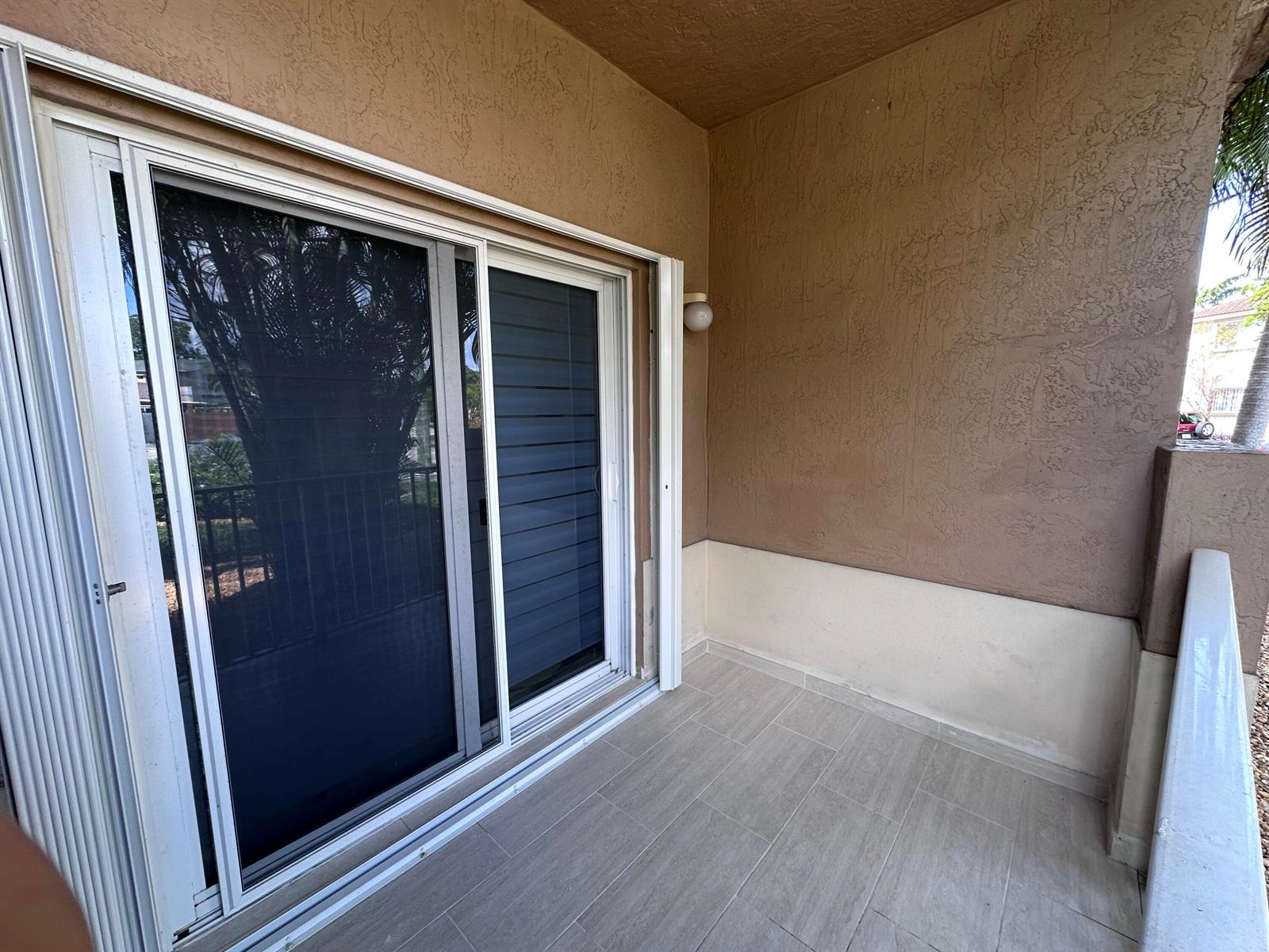 A covered balcony features tiled flooring, a sliding glass door, and textured brown walls — 300 E 4th Street # 103, Hialeah FL 33010, HIALEAH, FL