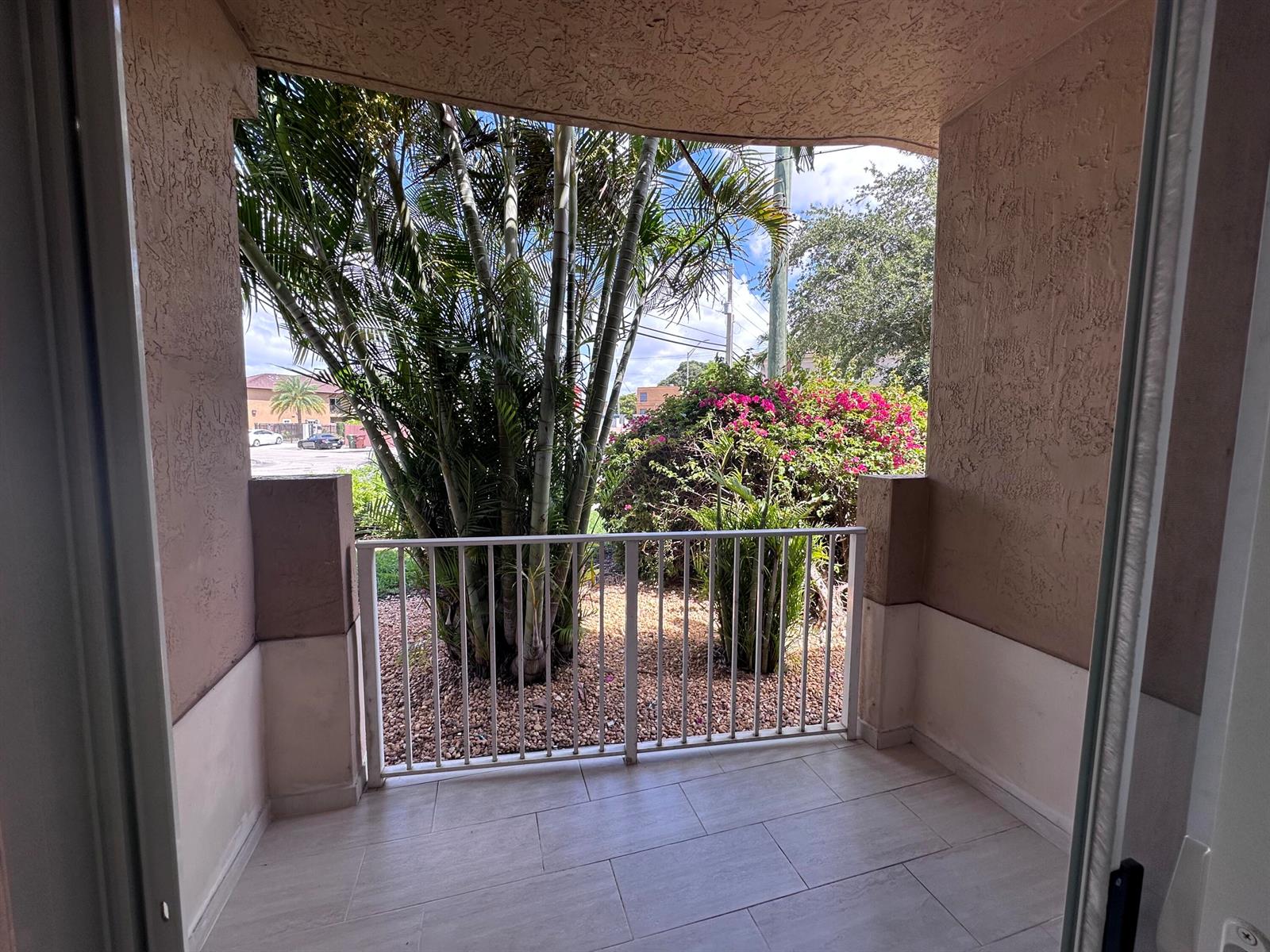 A covered patio with light tile flooring, a white metal railing, and views of landscaping — 300 E 4th Street # 103, Hialeah FL 33010, HIALEAH, FL