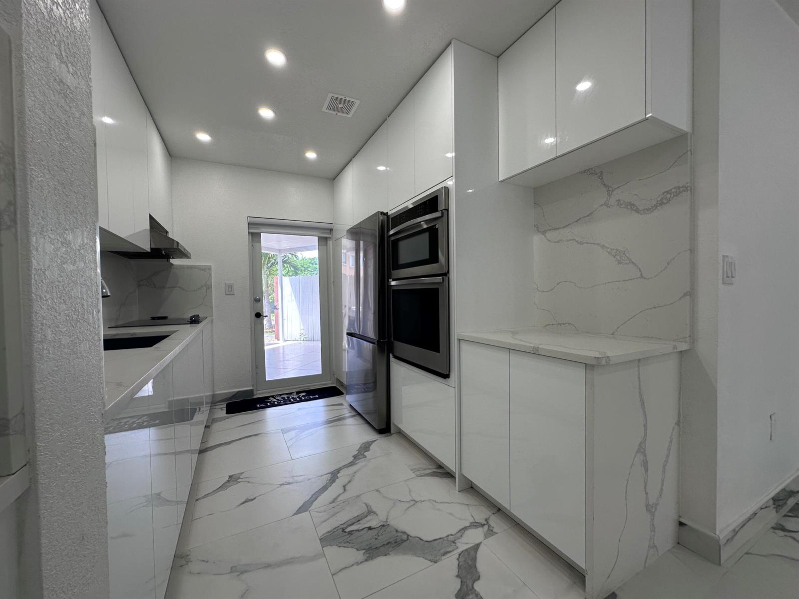 A modern white kitchen features marble-patterned tile floors, stainless steel appliances, and quartz countertops — 300 E 4th Street # 103, Hialeah FL 33010, HIALEAH, FL