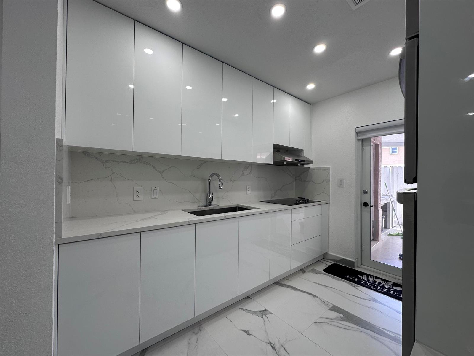 A modern kitchen features white high-gloss cabinets, marble-patterned countertops, a backsplash, and tile flooring — 300 E 4th Street # 103, Hialeah FL 33010, HIALEAH, FL