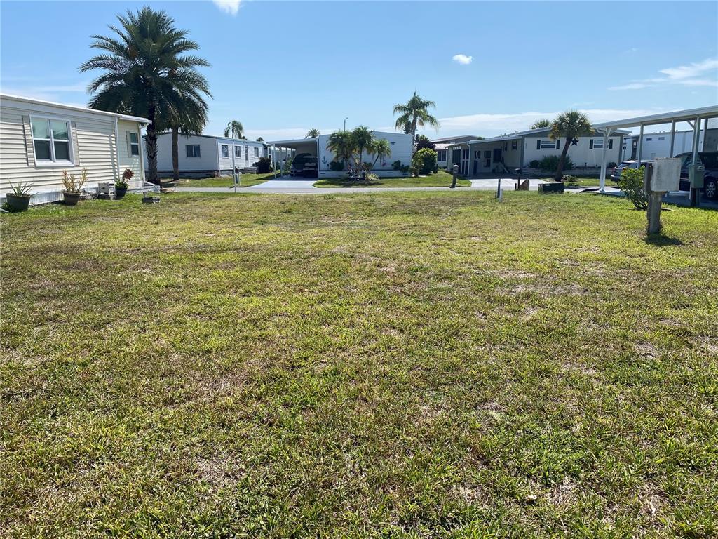 A vacant, grassy residential lot sits between several manufactured homes under a blue sky — 530 PARKWOOD AVENUE, NORTH PORT, FL