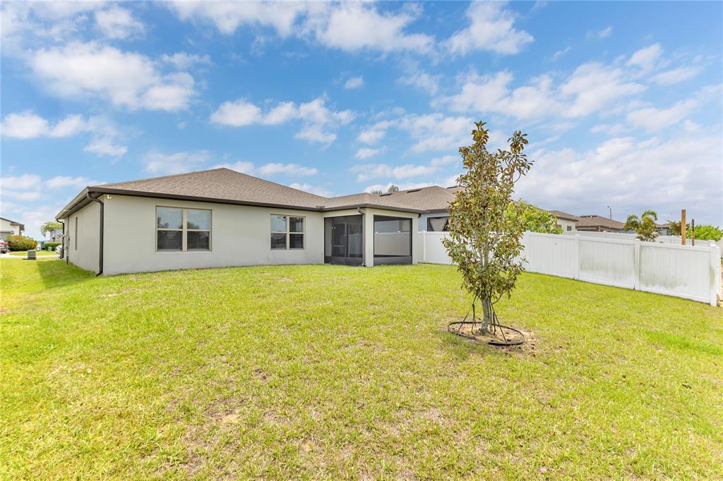 The backyard of a single-story house features a screened-in porch and a white fence — 747 CITRUS ISLE DRIVE, DAVENPORT, FL