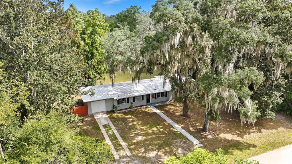 An aerial view shows a single-story house with a metal roof surrounded by large trees — 130 SW PEACH STREET, KEYSTONE HEIGHTS, FL
