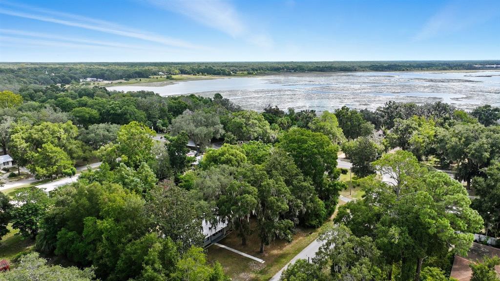 An aerial view shows a house nestled among dense trees near a large coastal marsh — 130 SW PEACH STREET, KEYSTONE HEIGHTS, FL