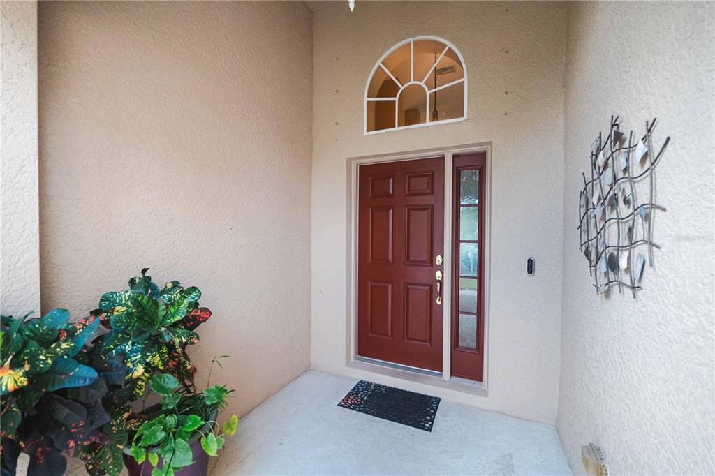 A red front door with a sidelight and arched transom window sits under a porch — 9020 N RIVER ROAD, TAMPA, FL