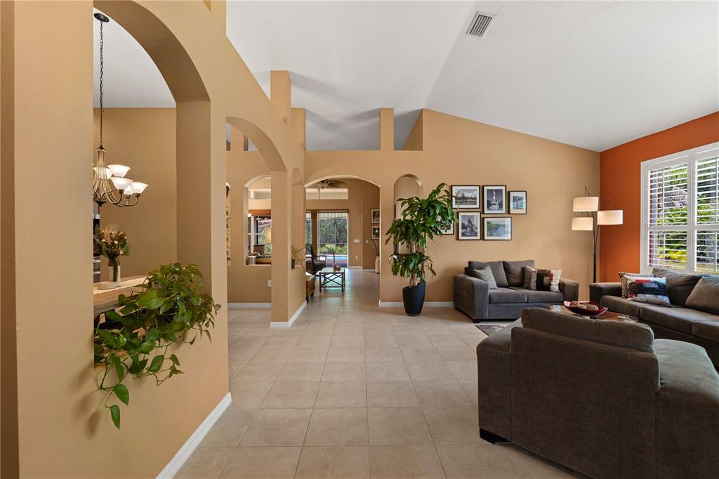 A living room with tan walls, tile flooring, arched doorways, and a vaulted ceiling — 9020 N RIVER ROAD, TAMPA, FL