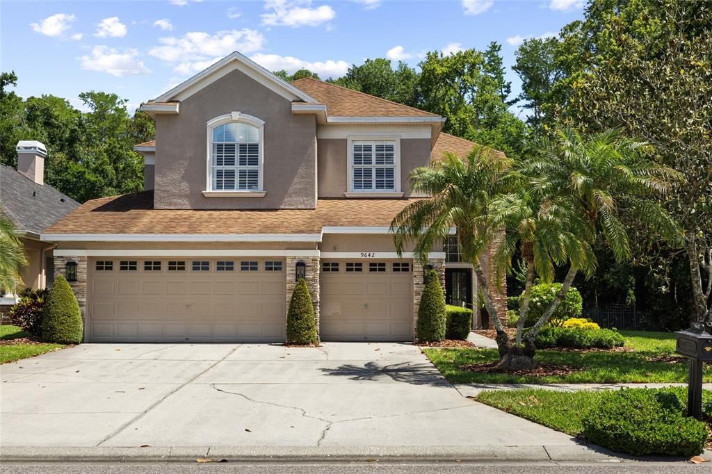 A two-story suburban house with a tan stucco exterior, brown roof, and three-car garage — 9642 GRETNA GREEN DRIVE, TAMPA, FL