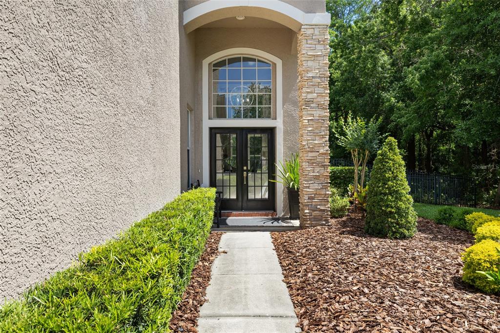 A concrete walkway leads to a double-door entrance with a stone pillar and arched window — 9642 GRETNA GREEN DRIVE, TAMPA, FL