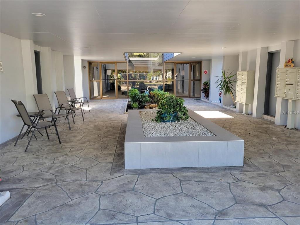 An open-air building entrance features a central stone planter, seating area, and mailboxes — 21320 BRINSON AVENUE UNIT 105, PORT CHARLOTTE, FL
