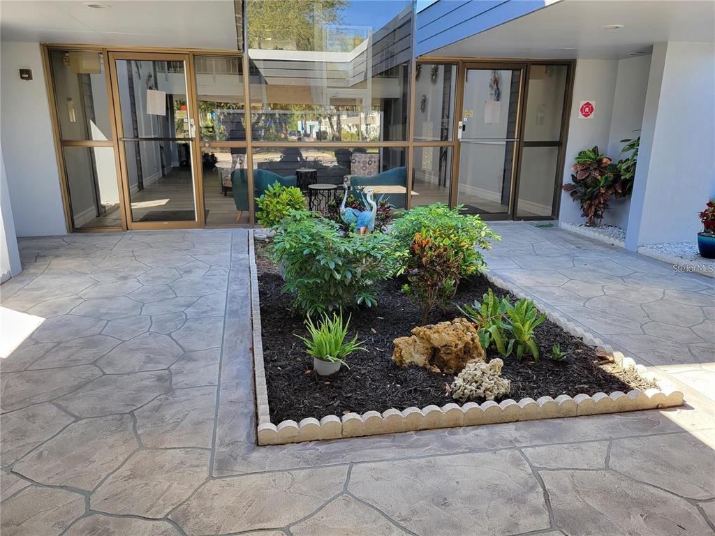 A landscaped garden bed sits in front of a building entrance with glass doors — 21320 BRINSON AVENUE UNIT 105, PORT CHARLOTTE, FL