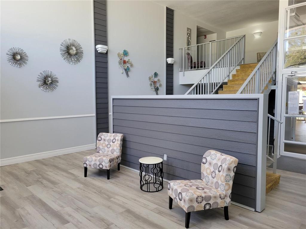 A lobby features two patterned chairs, a small side table, and a staircase with railings — 21320 BRINSON AVENUE UNIT 105, PORT CHARLOTTE, FL