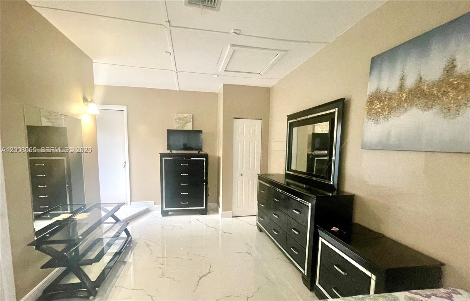 A bedroom features black furniture, a large mirror, and white marble-patterned tile flooring — 1537 NE 30th Ct # 0, Pompano Beach FL 33064, POMPANO BEACH, FL